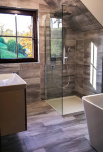 Foto eines neuen Badezimmers mit gläserner Dusche und marmorierten Wand- und Bodenfliesen.